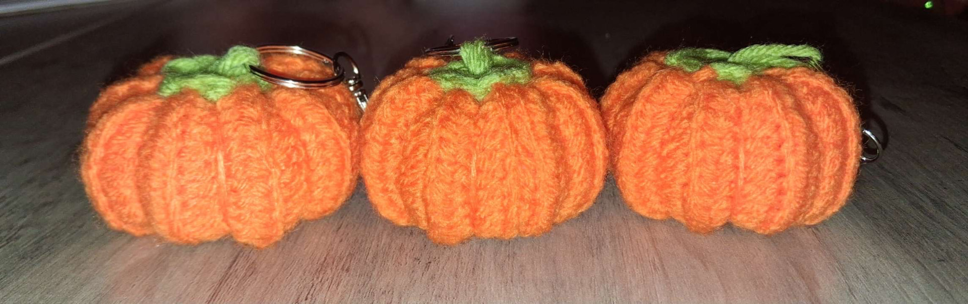 Three orange crocheted pumpkin keychains with green stems