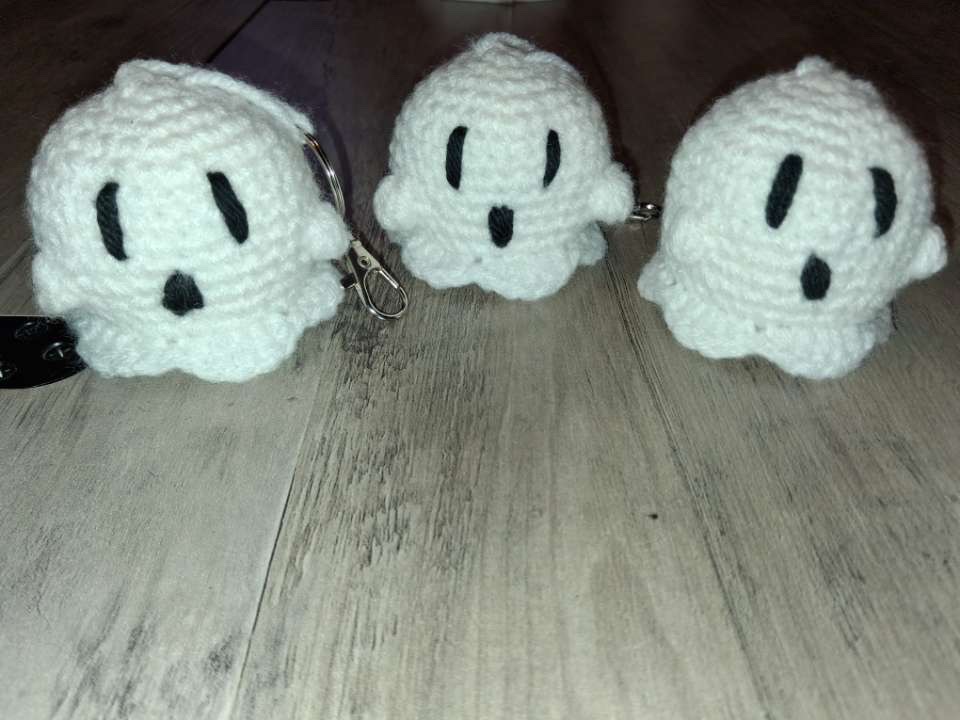 Three white crocheted ghost keychains with stitched eyes and mouths