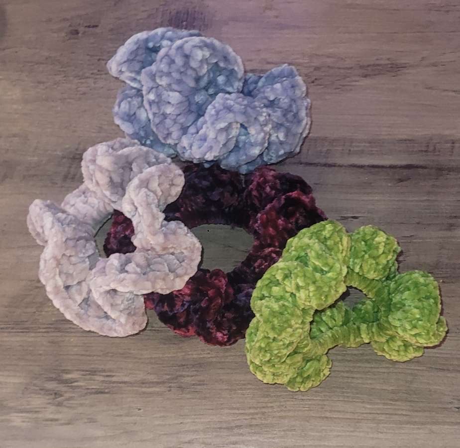 Four plush velvet crochet scrunchies in blue, grey, wine, and green