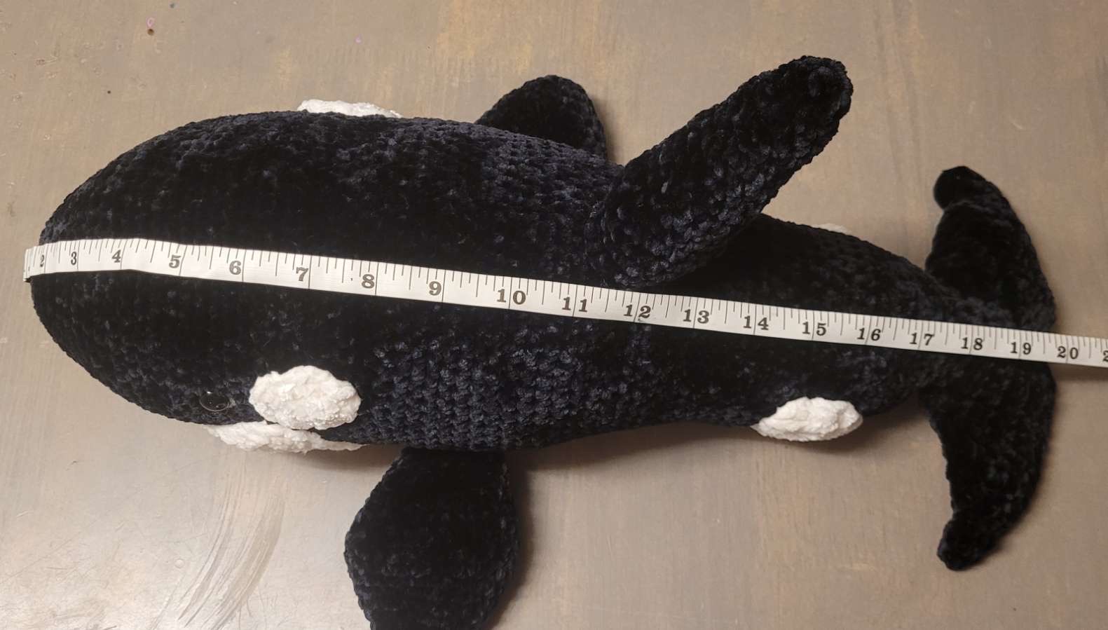Large black and white crocheted orca whale plush, approximately 20 inches long, shown with measuring tape